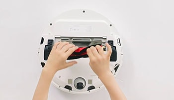 A woman cleans the vacuum's brushes.