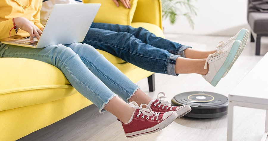 A robot vacuum cleaning the floor near the sofa and the young couple sitting on the sofa