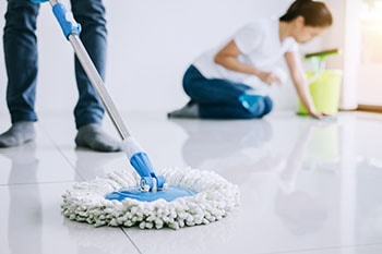 A married couple uses spin mop to clean the tile floor of their home.
