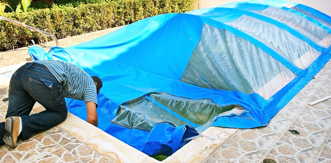 A man installing the pool cover for his pool.