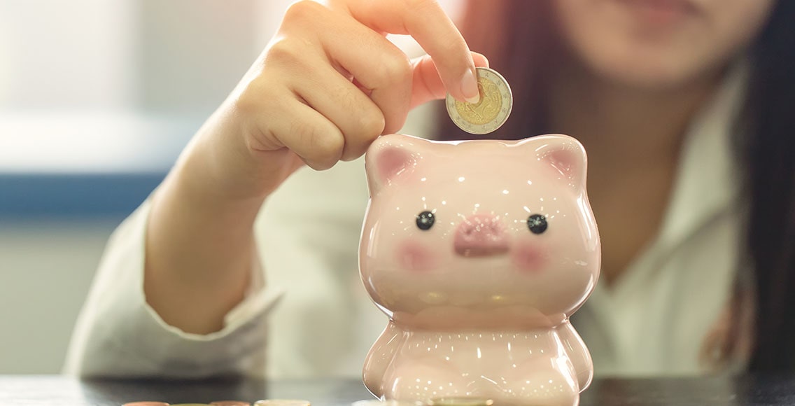 Young woman puts a coin into the piggy bank.