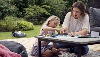 A woman and a girl playing together while robot lawn mower doing its job