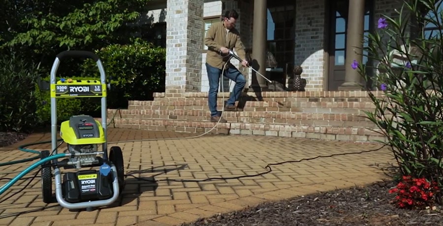 A man washes the front walkway of his house with the help of electric pressure washer from Ryobi.