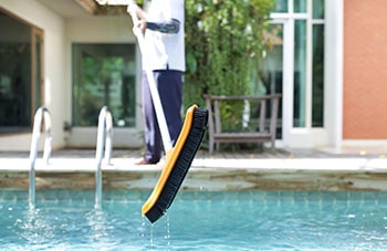 Man is scrubbing swimming pool walls with a brush.