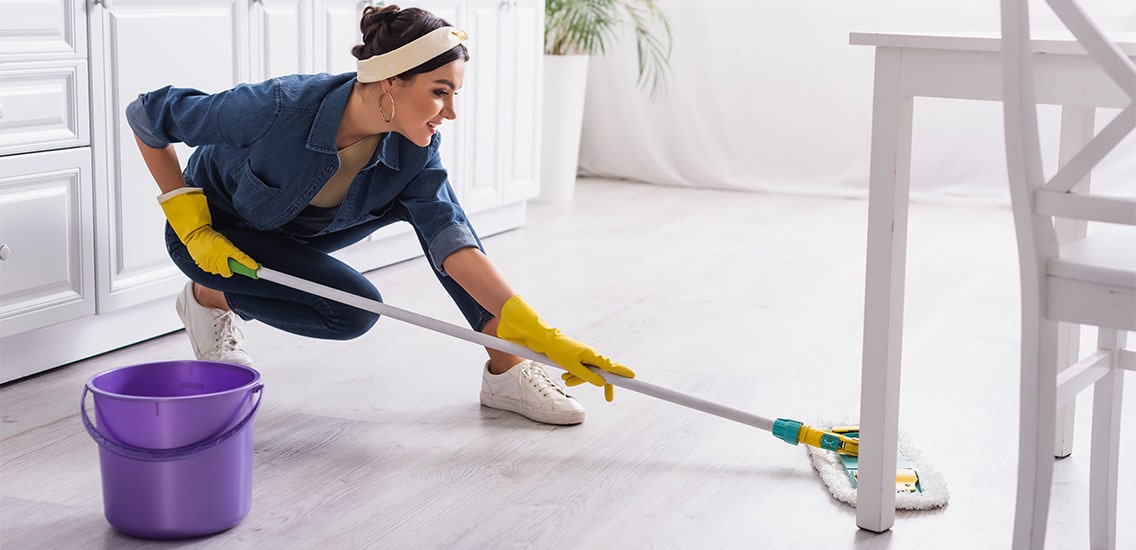 A pretty woman mops the kitchen floor.