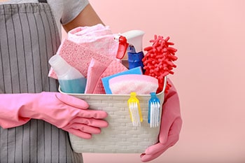Woman holding basket with cleaning supplies.