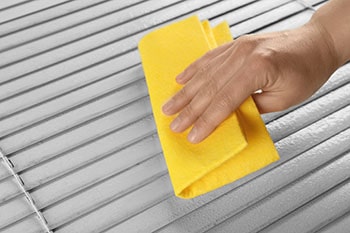 Hand cleaning dirty window blinds.
