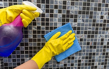 Woman cleans a tile wall with the cloth and cleaner.