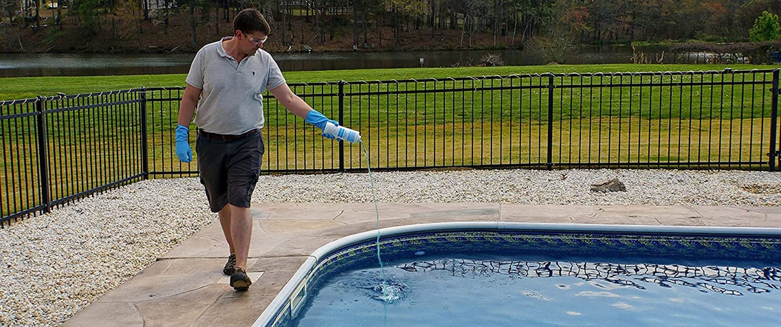 Man pours algaecide to the outdoor swimming pool