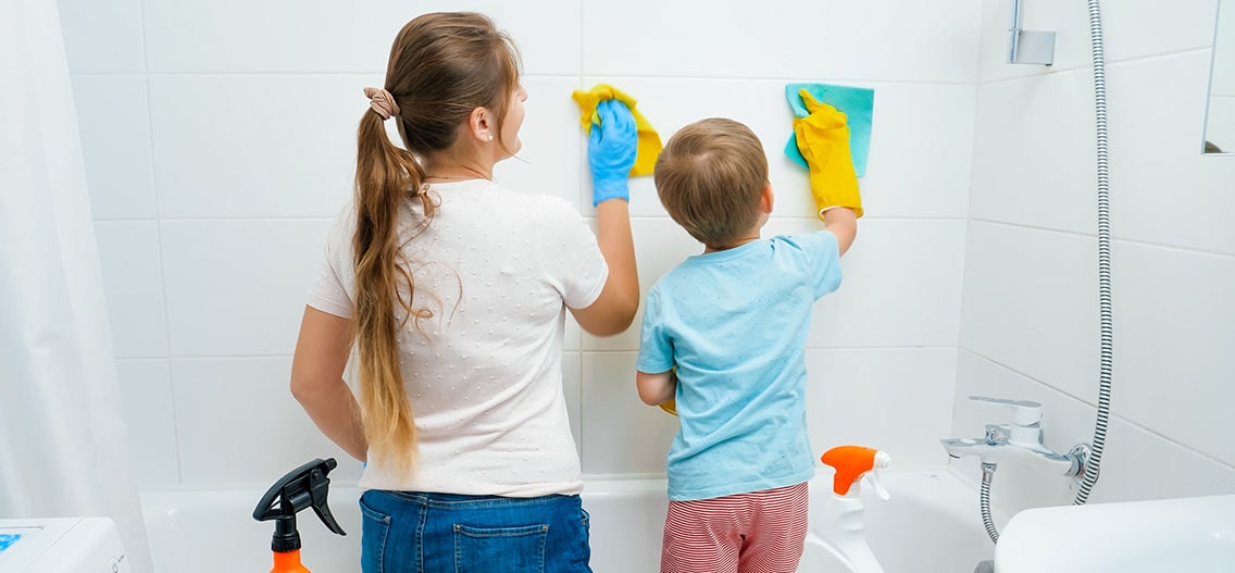 Little boy with mother washing and cleaning tile walls in a bathroom.