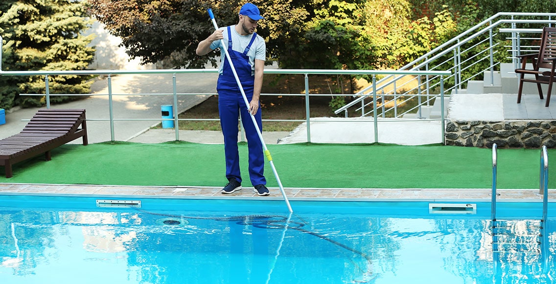 Man worker cleaning outdoor pool using manual pool vacuum.