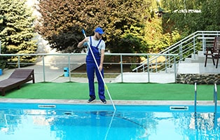 Man worker cleaning outdoor pool using manual pool vacuum